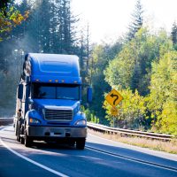 Blue semi truck and flat bed trailer on sunny green and gold aut